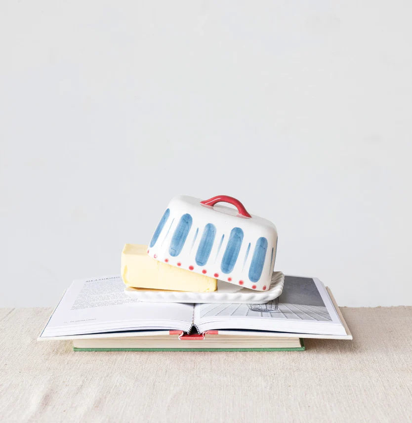 A hand painted butter dish with butter inside on top of books on a neutral background.