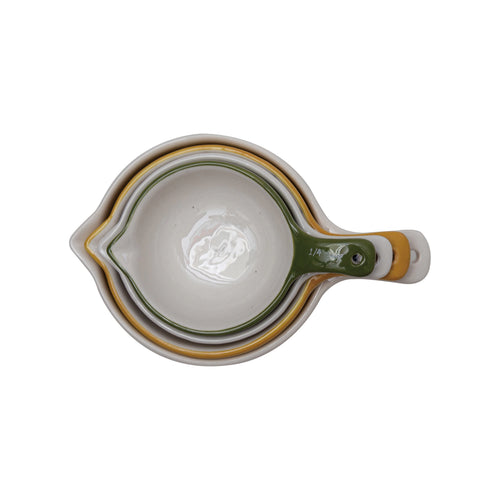 Set of four ceramic measuring cups with green handles on a white background