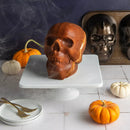 Skull-shaped cake on a white stand with pumpkins and a dark background