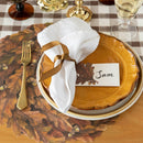 Thanksgiving table setting with gold plates, white napkin, and name card on a checkered tablecloth.