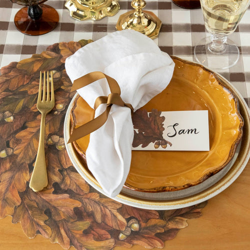 Thanksgiving table setting with gold plates, white napkin, and name card on a checkered tablecloth.