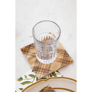 A glass atop a brown, orange, and yellow plaid napkin on a neutral surface.