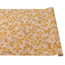 A rolled out paper table runner with a cherry blossom floral pattern in yellow and gold colors on a beige background.