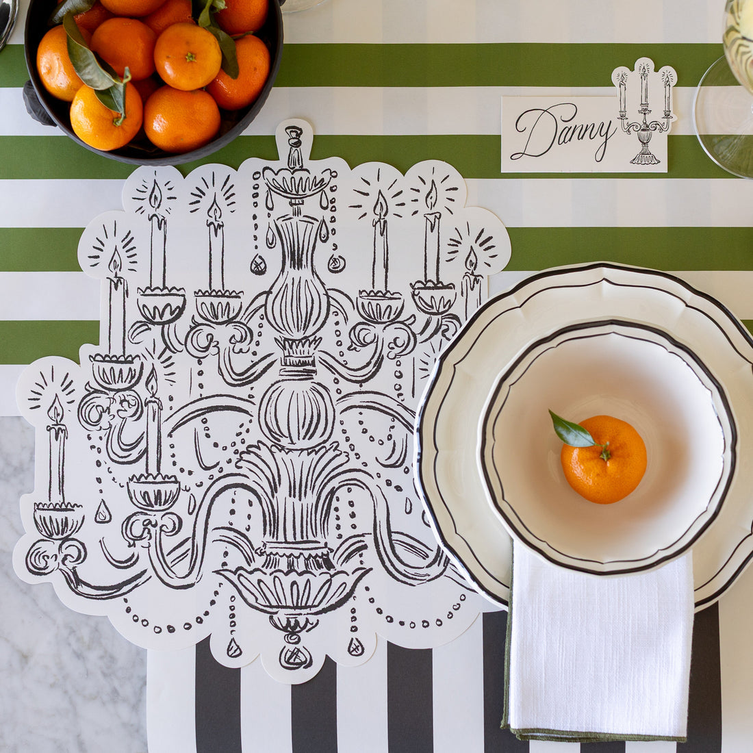 Placemat with chandelier design, bowl with orange, and striped tablecloth.