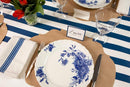 A blue and white striped table runner with a place setting featuring name card, French frame placemat, and blue and white plates and napkins with flowers in the corner.