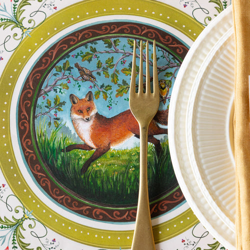 Decorative placemat with a fox design, with a gold fork, and paper plates on a colorful background