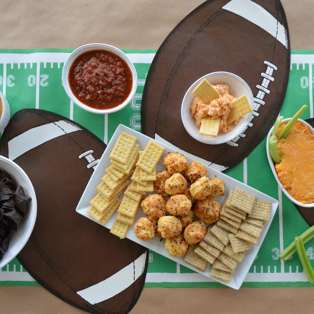 A football field table runner with football shaped placemats and bowls and plates of food on top of it.