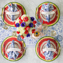 Four place settings on a table with a blue and white table runner, paper watermelon placemats, name cards, drinkware, flatware, plates, blue and white napkins, and floral centerpiece.