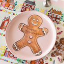 Gingerbread man cookie with 'happy holidays' on a pink plate, colorful gingerbread-themed background