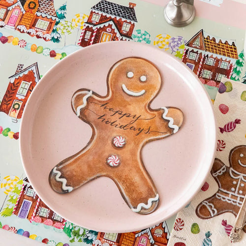 Gingerbread man cookie with 'happy holidays' on a pink plate, colorful gingerbread-themed background