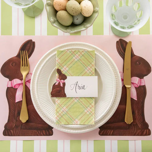 Easter-themed place setting with chocolate bunny placemats and a name card on a striped tablecloth.
