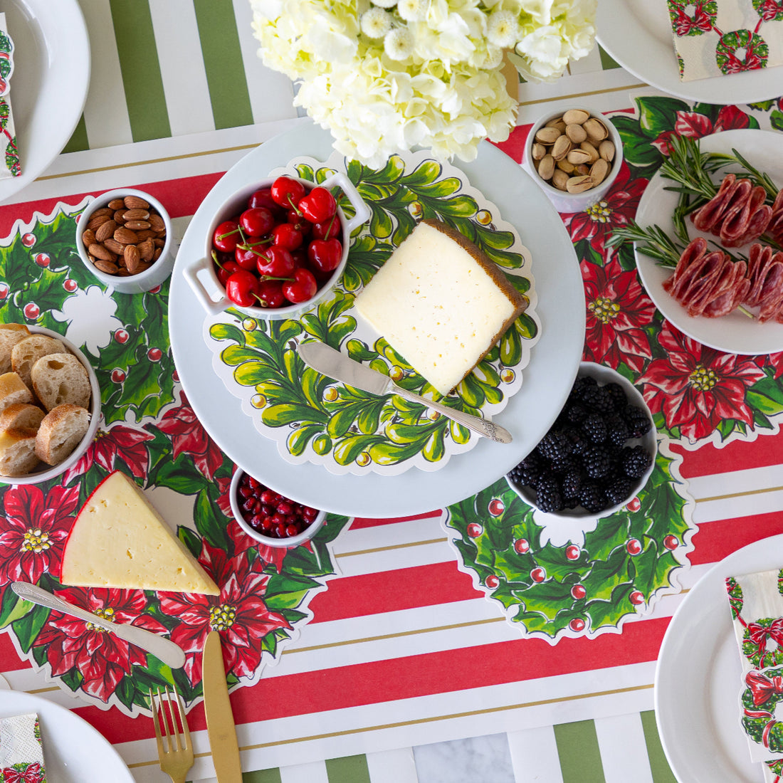 Table setting with Christmas-themed placemats, cheese, fruits, and nuts on a festive tablecloth.