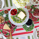Table setting with Christmas-themed placemats, cheese, fruits, and nuts on a festive tablecloth.