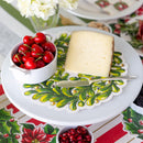Block of cheese with cherries on a decorative plate with a Christmas-themed tablecloth.