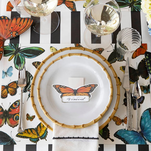 A place setting with butterfly placemat, name card, and black and white striped table runner.