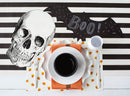 A black and white striped table runner topped with Halloween decor and a place setting.