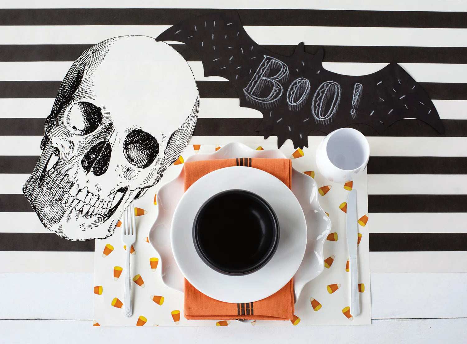 A black and white striped table runner topped with Halloween decor and a place setting.