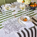 A table setting with chandelier art paper placemats, green striped table runner, black and white striped table runner, glasses of wine and oranges in a bowl.