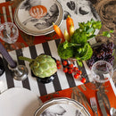 Fruit and vegetables on a table with a black and white striped table runner and autumn themed place settings.