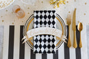 A black, gold, and white styled place setting with checkered napkin, gold flatware, and starry table runner.