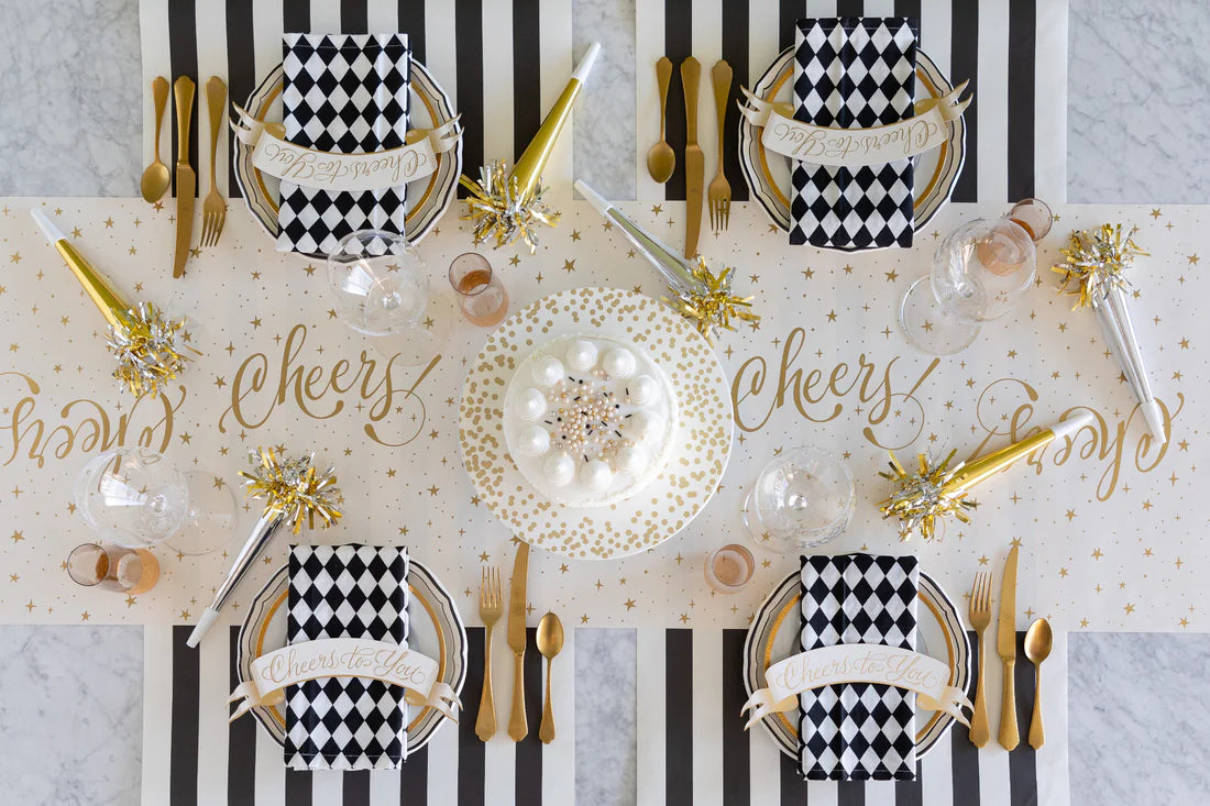 A celebratory place setting with a "cheers" table runner, black and white decor, napkins, and cake.