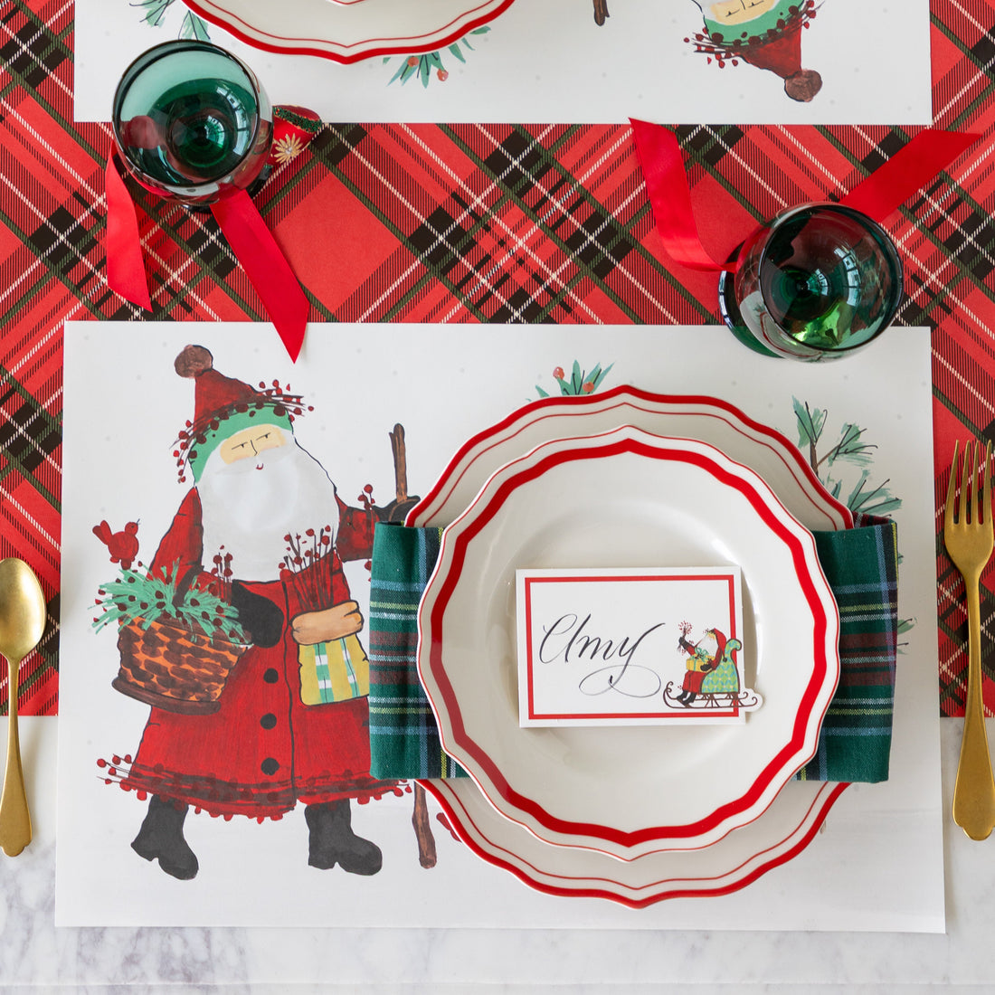 Christmas-themed table setting with Santa Claus placemat, decorative plates, and Santa name card.