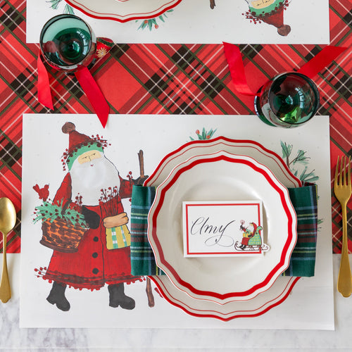 Christmas-themed table setting with Santa Claus placemat, decorative plates, and Santa name card.