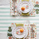 Table setting with floral placemats, white plates, and cutlery on a striped tablecloth.