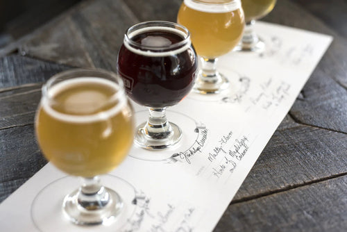 A set of drinks on tasting papers on a wooden surface.