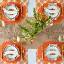 A table set for Thanksgiving with a brown table runner with "thankful" in script, flowers in the center, and four place settings with orange accents and place cards shaped like banners with 'thankful for you' written on them.
