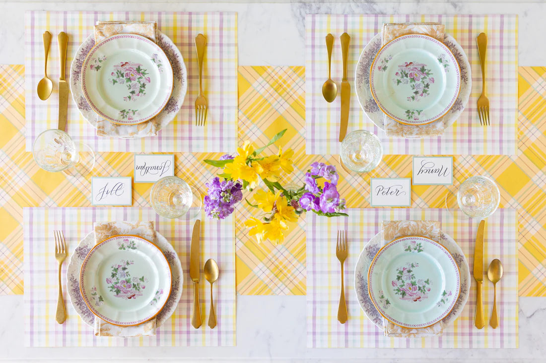 Elegant table setting with floral plates, gold cutlery, and yellow plaid tablecloth.