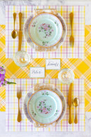 Elegant table setting with floral plates, gold cutlery, and a yellow checkered tablecloth.