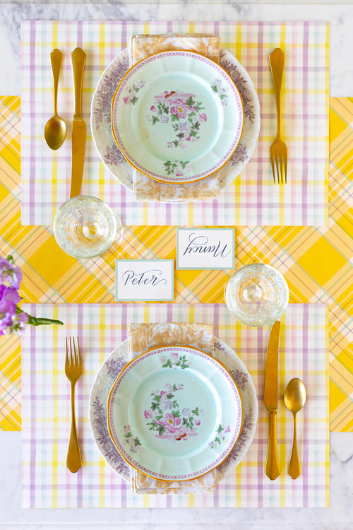 Elegant table setting with floral plates, gold cutlery, and a yellow checkered tablecloth.