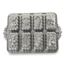 A silver metal holiday baking pan with eight decorative mold cavities shaped like Christmas treats, including a candy cane, Santa, gift box, and snowman, shown on a white background.