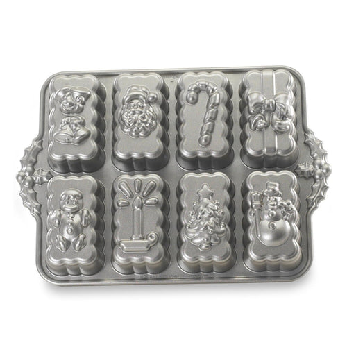 A silver metal holiday baking pan with eight decorative mold cavities shaped like Christmas treats, including a candy cane, Santa, gift box, and snowman, shown on a white background.