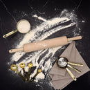 Baking tools including a rolling pin, measuring cups, and flour on a dark surface.