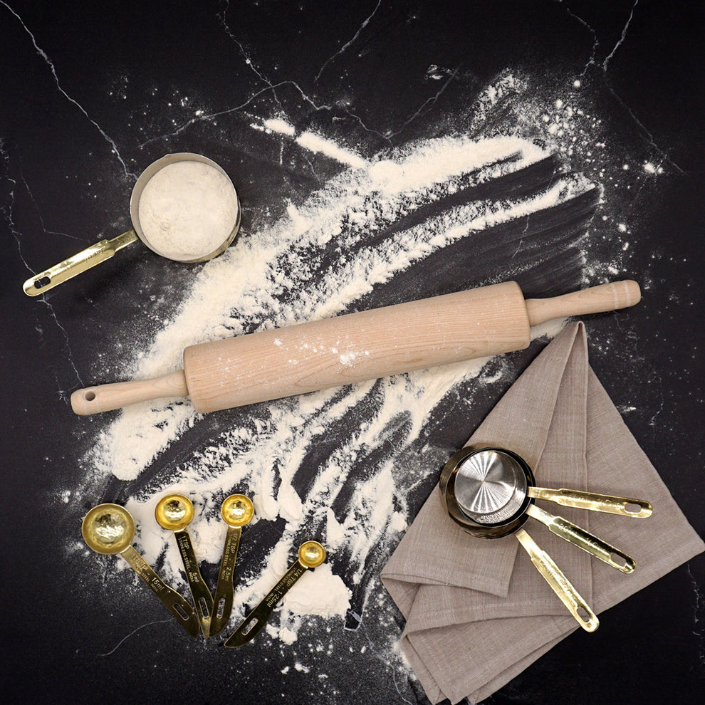 Baking tools including a rolling pin, measuring cups, and flour on a dark surface.