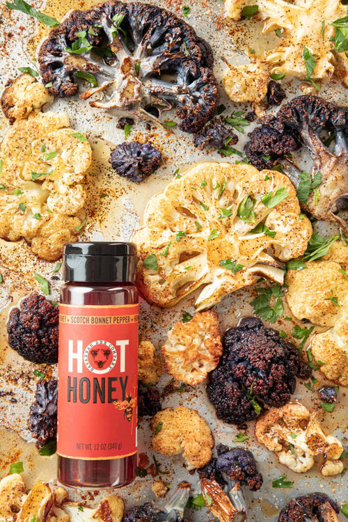 Roasted cauliflower with a bottle of Hot Honey on a baking sheet.