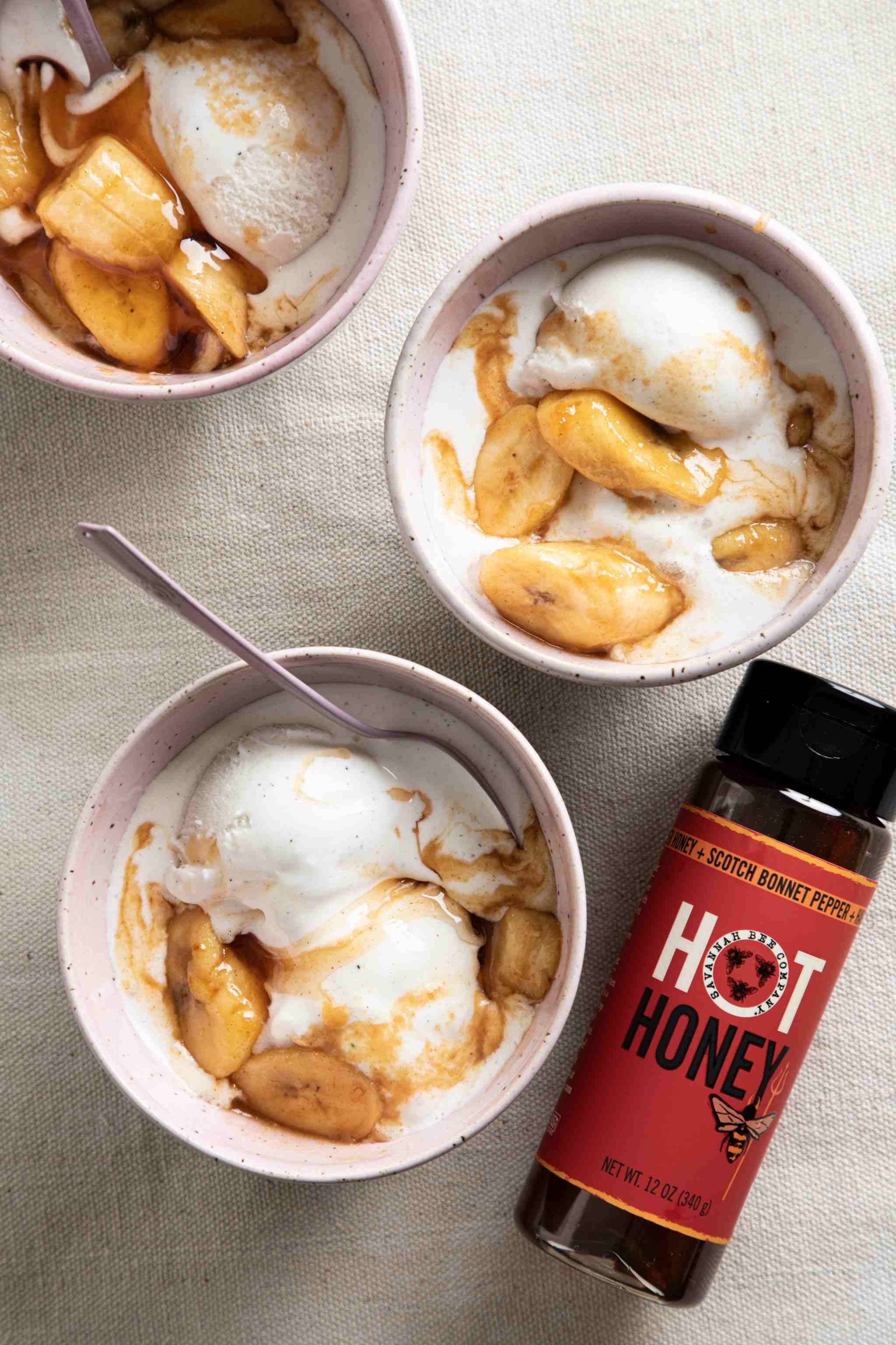 Three bowls of ice cream with hot honey drizzle on a textured surface, accompanied by a bottle of hot honey.