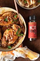Baked chicken with hot honey glaze in a dish on a wooden table with a bottle of hot honey.