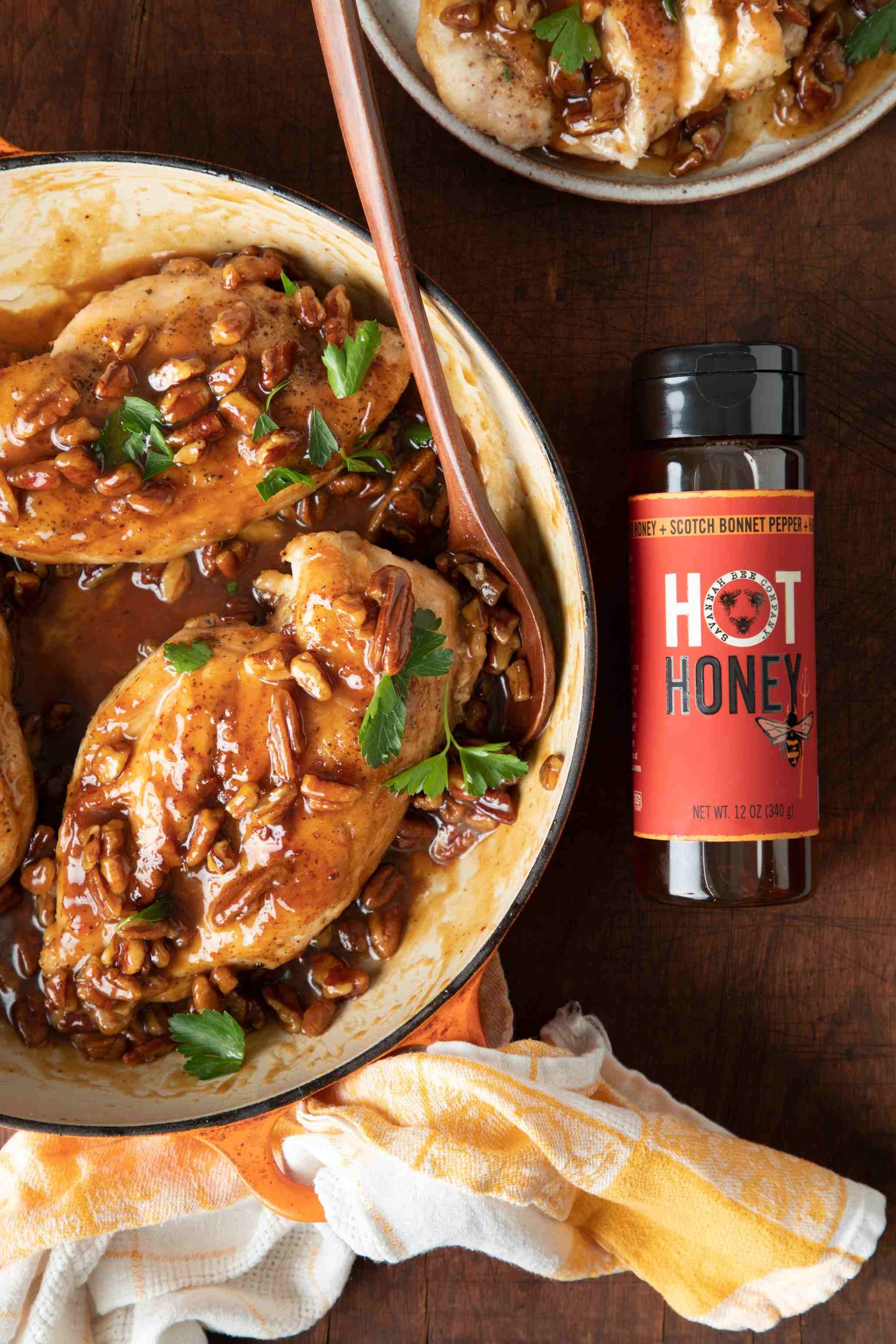 Baked chicken with hot honey glaze in a dish on a wooden table with a bottle of hot honey.