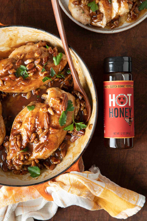 Baked chicken with hot honey glaze in a dish on a wooden table with a bottle of hot honey.