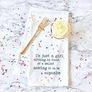 Kitchen towel with text on a marble surface with a gold fork, cupcake, and sprinkles.