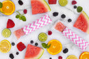 Ice pops in pink and white zigzag holders on a marble surface with fruit slices, berries, and watermelon slices.