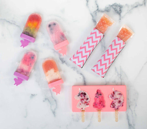A set of finished ice pops in different shapes and unicorn molds on a marble surface.