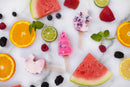 Unicorn shaped ice pops on a marble surface with fruit slices, berries, and watermelon slices.