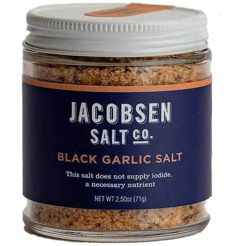 A clear glass jar with a white lid containing black garlic salt, labeled Jacobson Salt Co. Black Garlic Salt.
