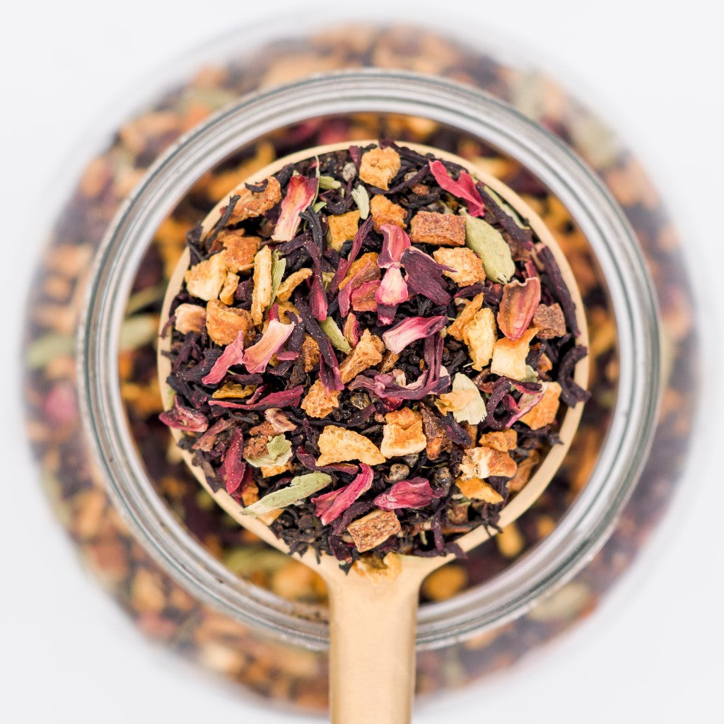 Wooden spoon filled with colorful dried tea leaves over a glass jar.