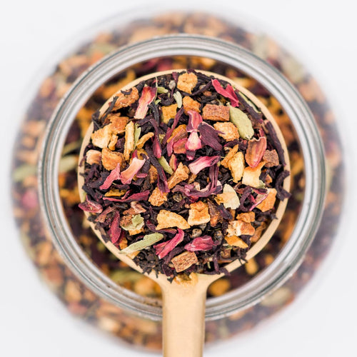 Wooden spoon filled with colorful dried tea leaves over a glass jar.
