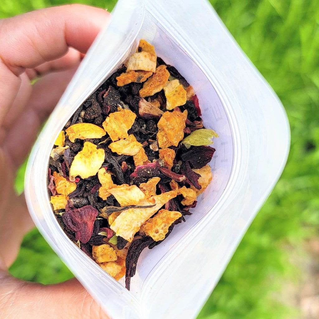 Hand holding a container of tea mix  against a green outdoor background